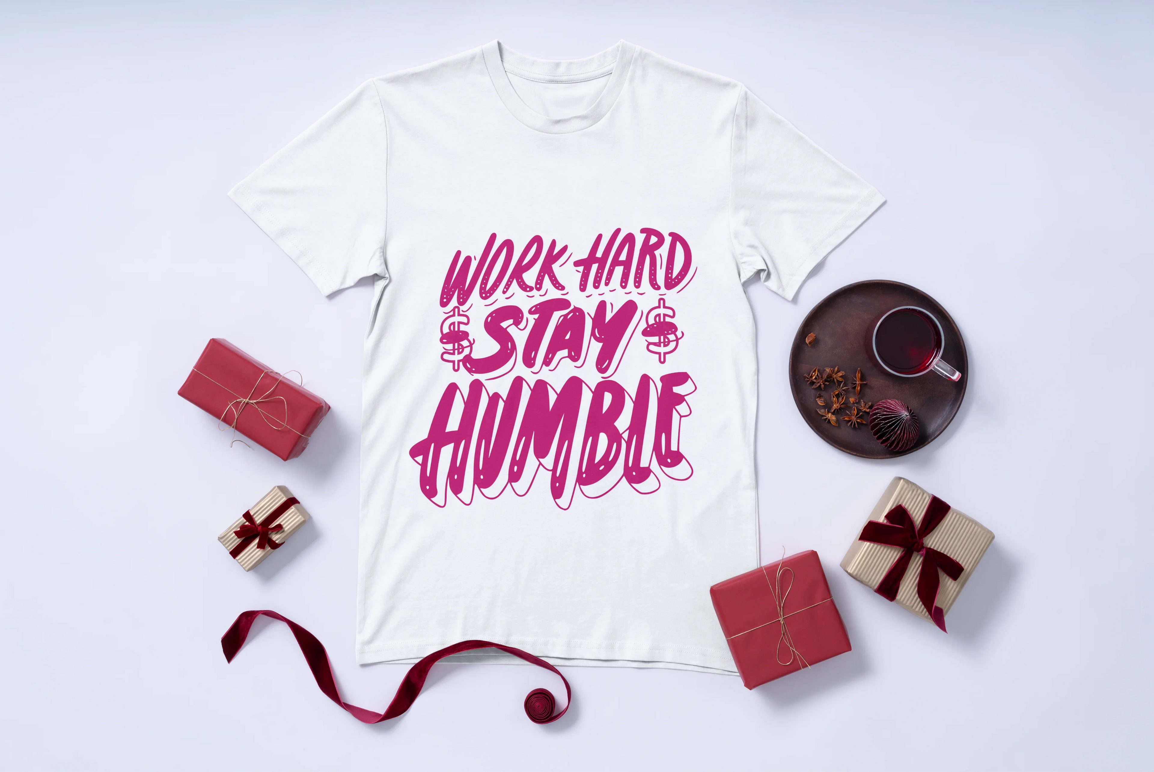 White t-shirt with 'Work Hard Stay Humble' text in pink color on a white background with decorative items.