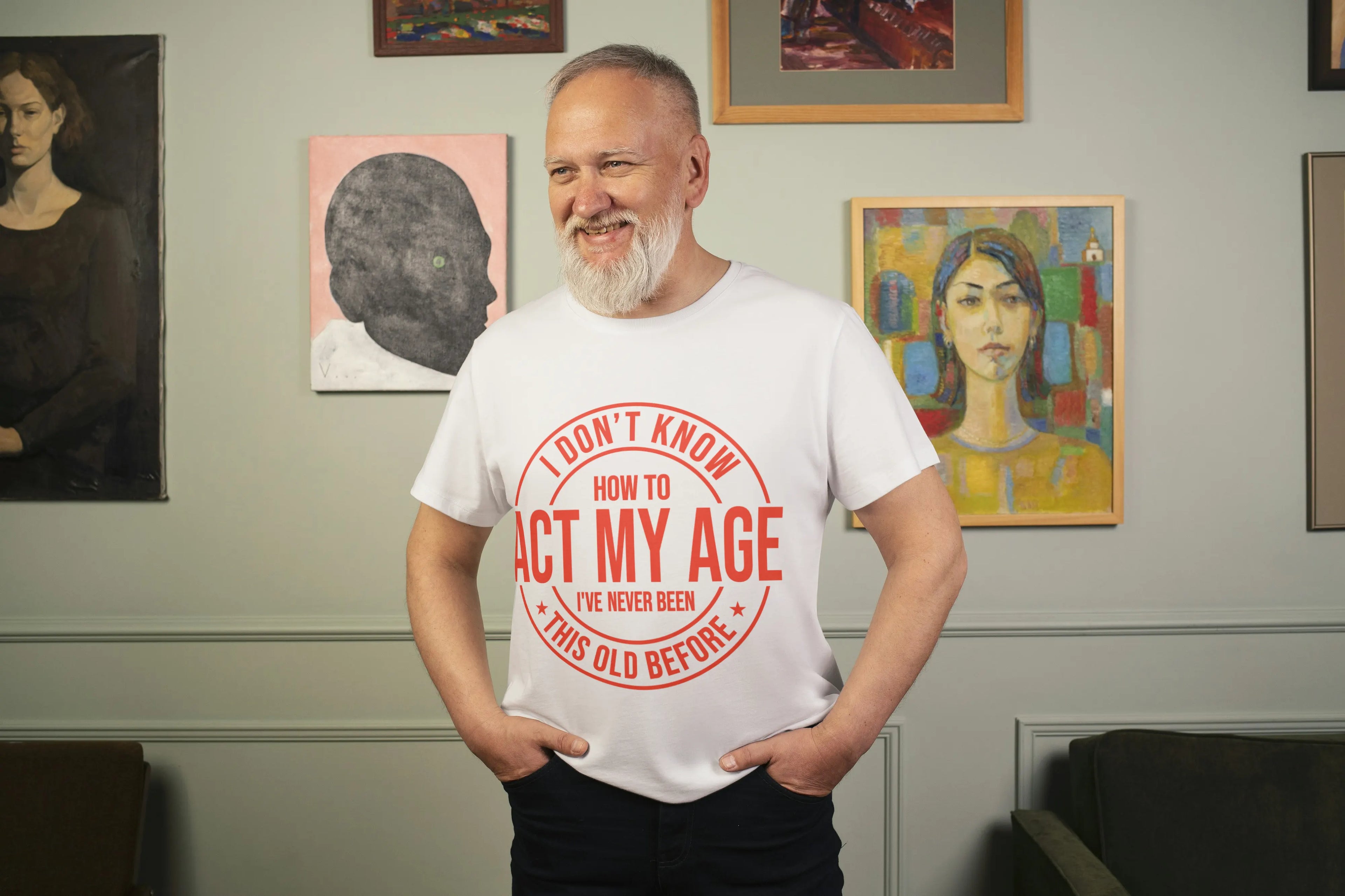 Man wearing a white t-shirt with red text in a room with framed artworks on the wall.