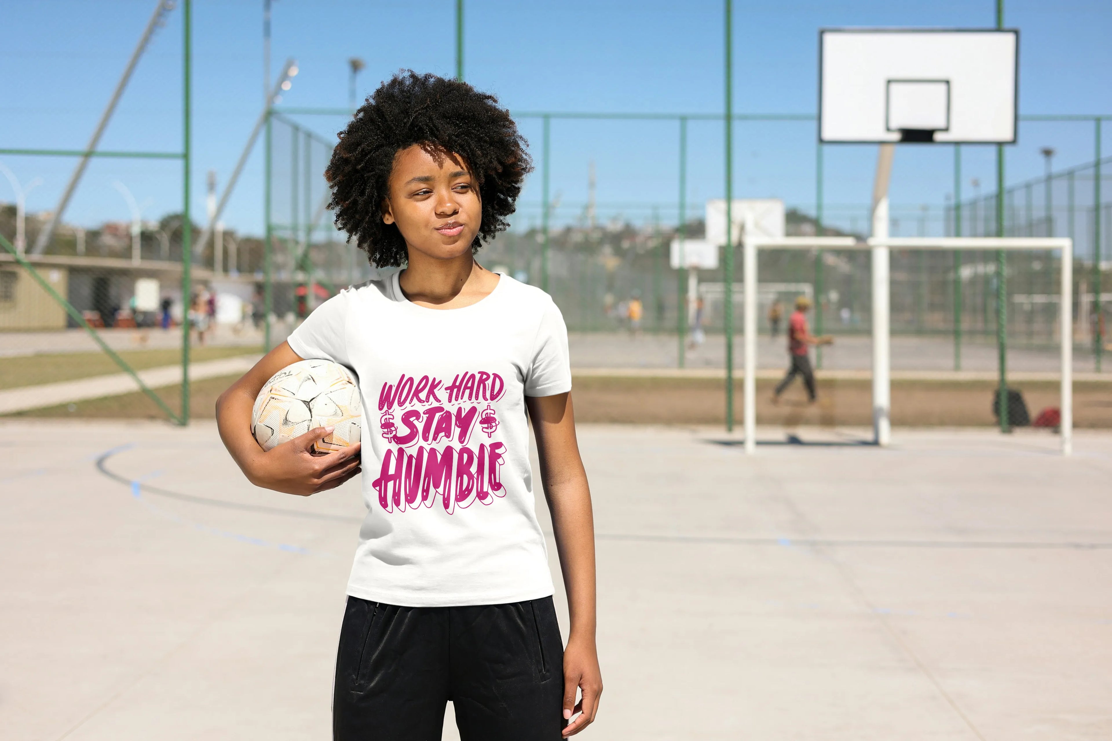 Person holding a volleyball on a sports court wearing a t-shirt with motivational text Work Hard Stat Humble in pink color