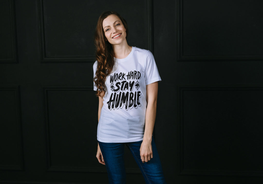 Woman wearing a white t-shirt with 'Work Hard Stay Humble' text against a dark background